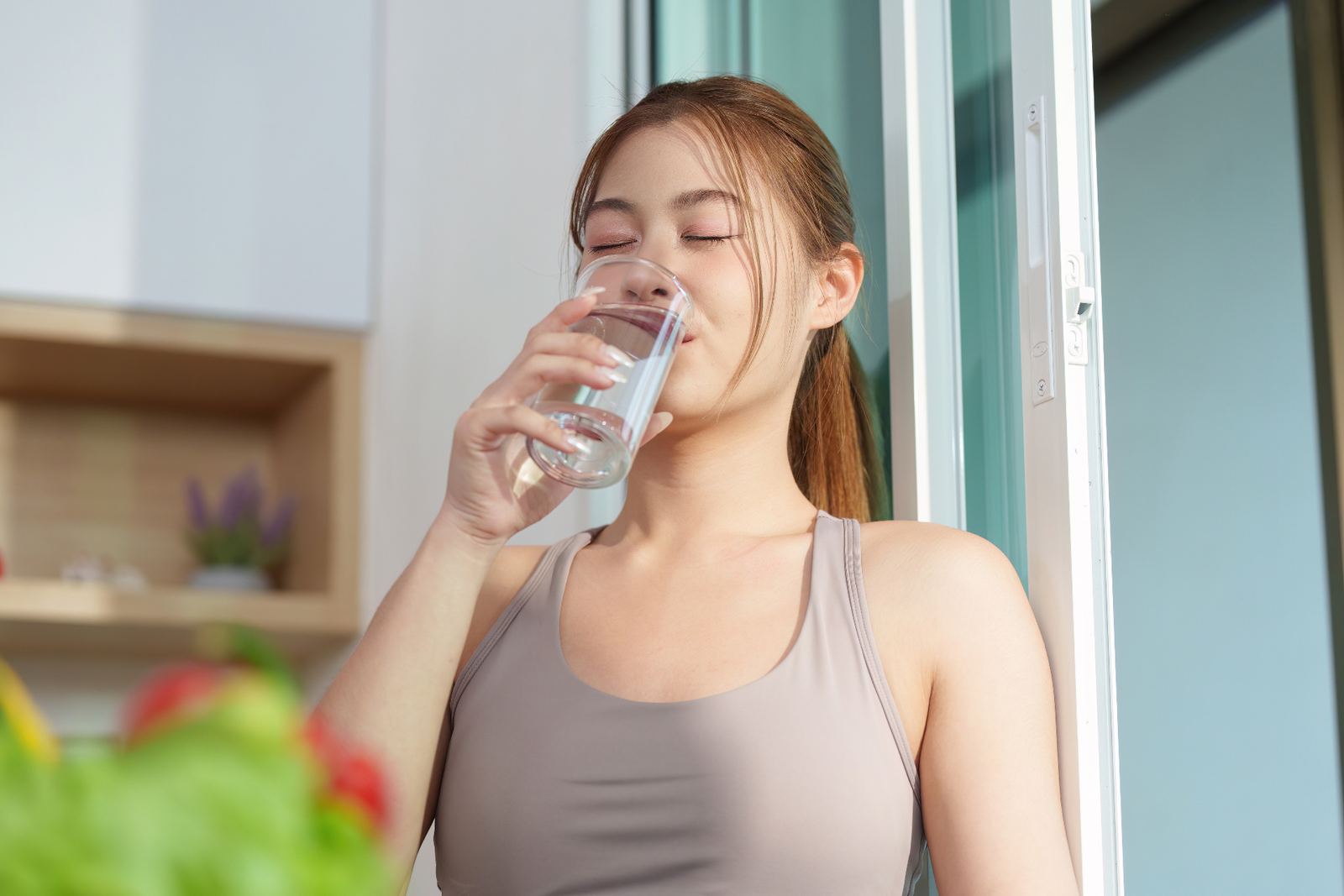 Woman drinking clean filtered water in a bright kitchen